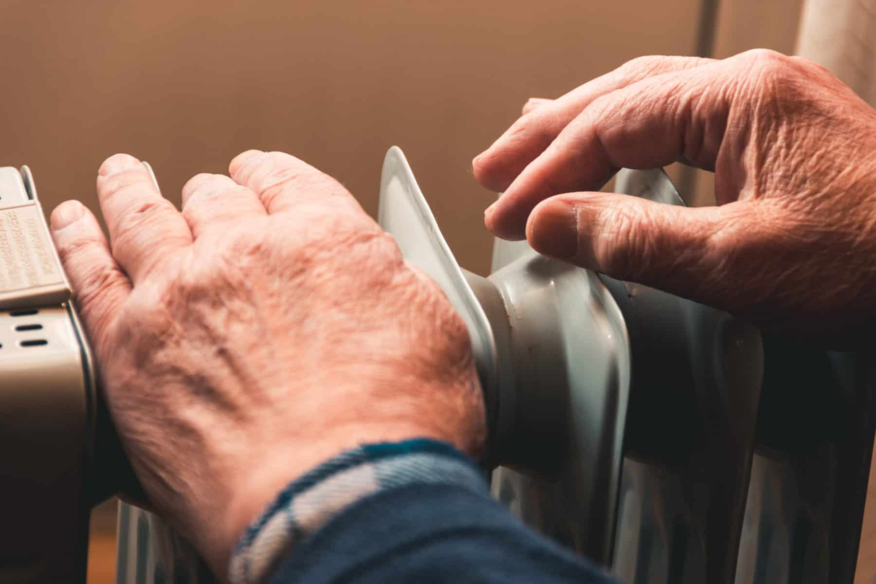 Un anciano se calienta las manos sobre un calentador eléctrico. Fuera de temporada, la calefacción central se retrasa, por lo que la gente tiene que comprar calentadores adicionales para mantener las casas calientes a pesar del aumento de las facturas de electricidad. El calentador paga menos que la luz.