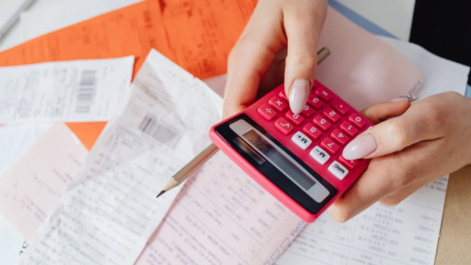 Imagen de facturas y persona haciendo matemáticas con una calculadora.